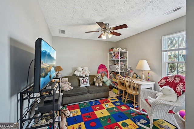 living area with ceiling fan, a textured ceiling, and visible vents