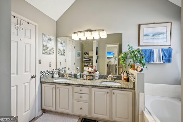 bathroom featuring vaulted ceiling, double vanity, tiled bath, and a sink