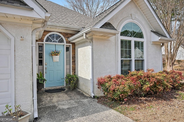 entrance to property featuring roof with shingles and stucco siding