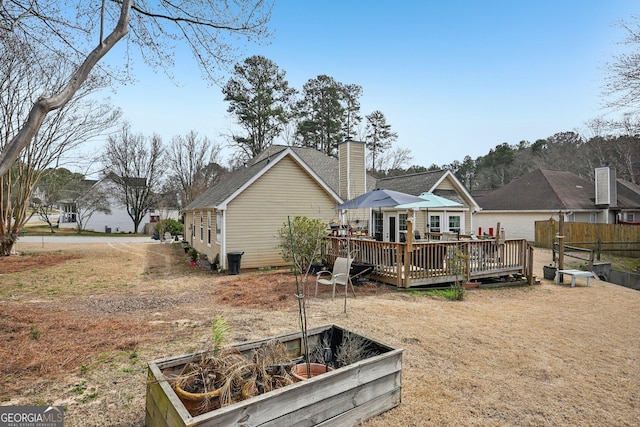 back of property with a garden, a chimney, fence, and a deck