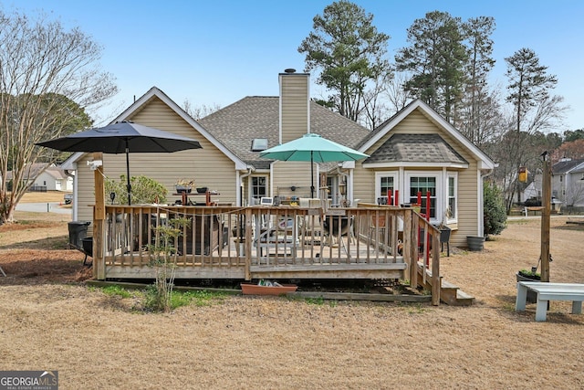 rear view of house featuring a shingled roof, a chimney, and a wooden deck