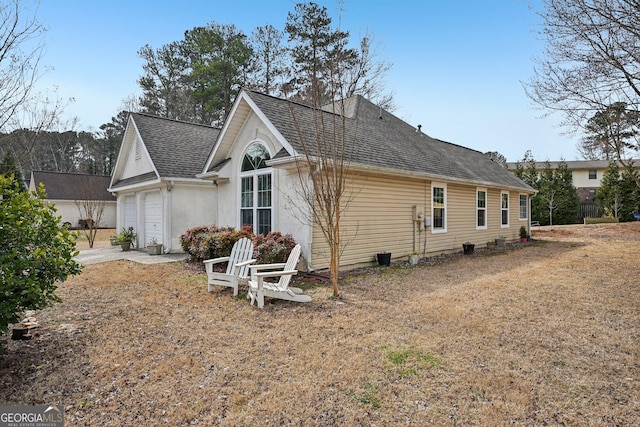 back of property with driveway, a shingled roof, and a garage