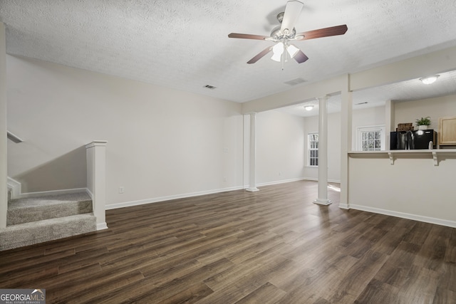 unfurnished living room featuring ornate columns, stairway, dark wood finished floors, and a textured ceiling