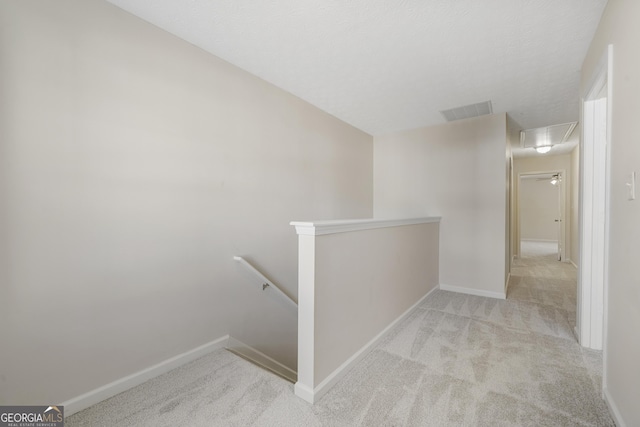 hallway featuring attic access, visible vents, carpet flooring, and an upstairs landing