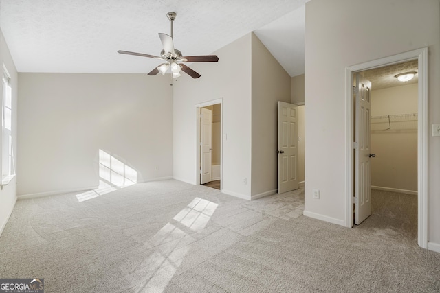 unfurnished bedroom featuring a walk in closet, carpet flooring, vaulted ceiling, a textured ceiling, and baseboards