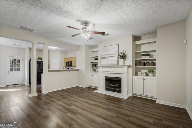 unfurnished living room featuring dark wood-type flooring, a high end fireplace, baseboards, visible vents, and ornate columns