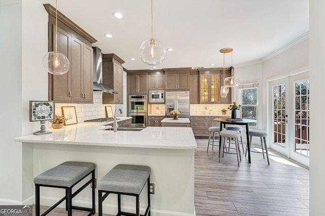 kitchen with decorative backsplash, wall chimney exhaust hood, built in appliances, a peninsula, and french doors