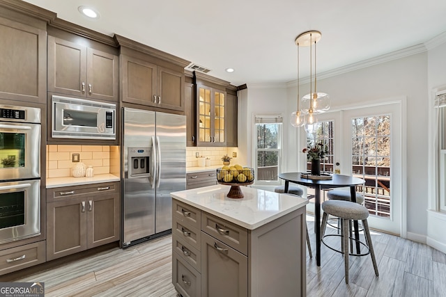 kitchen with tasteful backsplash, glass insert cabinets, appliances with stainless steel finishes, ornamental molding, and pendant lighting