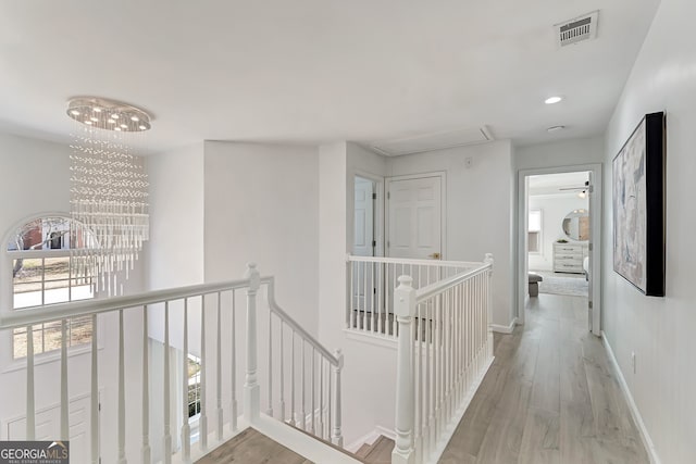 hallway with visible vents, an inviting chandelier, attic access, an upstairs landing, and wood finished floors