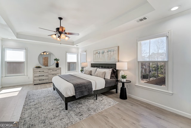 bedroom with a tray ceiling, multiple windows, and visible vents