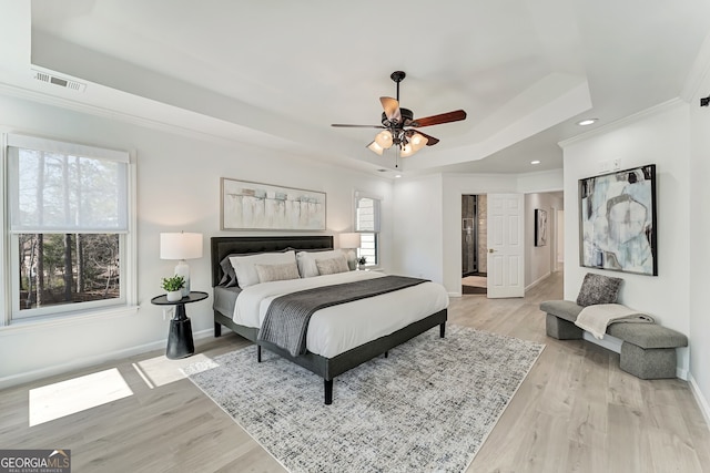 bedroom featuring visible vents, baseboards, a tray ceiling, light wood finished floors, and crown molding