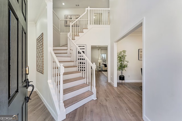 foyer featuring a towering ceiling, stairs, baseboards, and wood finished floors