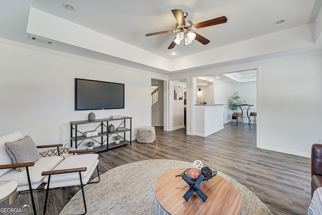 living room with a tray ceiling, crown molding, baseboards, and wood finished floors