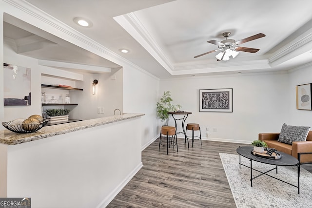 sitting room featuring baseboards, a tray ceiling, wood finished floors, and ornamental molding