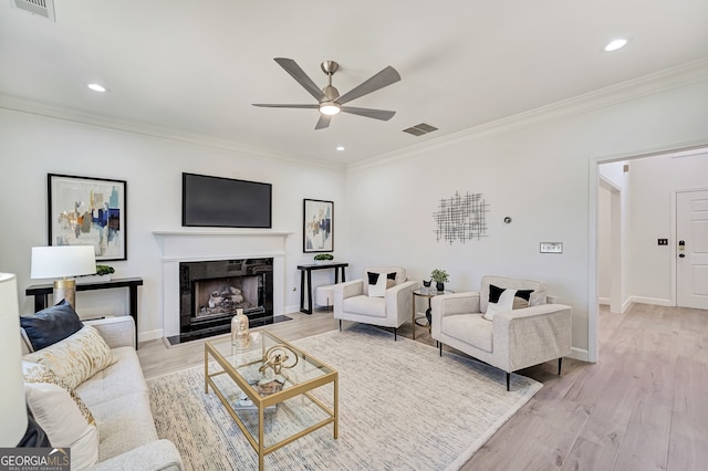 living room with ornamental molding, visible vents, a fireplace, and light wood-style flooring