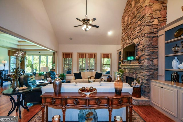 living area with a fireplace, high vaulted ceiling, wood finished floors, and ceiling fan with notable chandelier