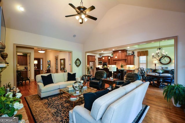 living room with high vaulted ceiling, ceiling fan with notable chandelier, and wood finished floors