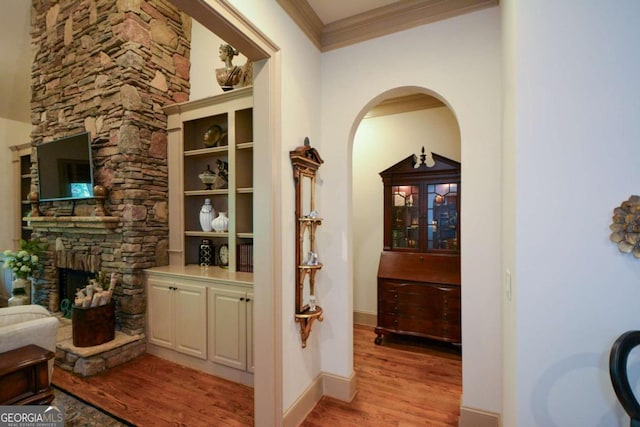 corridor featuring light wood finished floors, baseboards, ornamental molding, and arched walkways