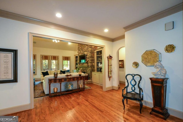 corridor featuring arched walkways, recessed lighting, baseboards, light wood finished floors, and crown molding