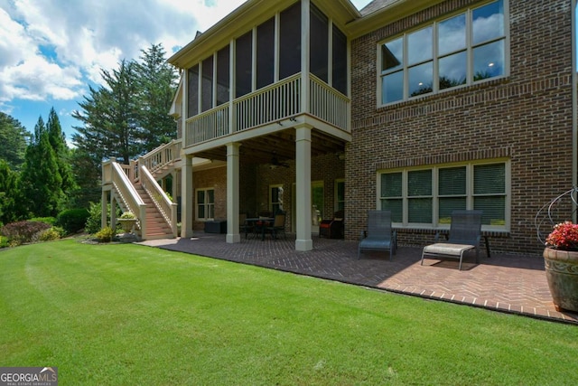 rear view of property with a patio, a sunroom, stairs, a yard, and brick siding