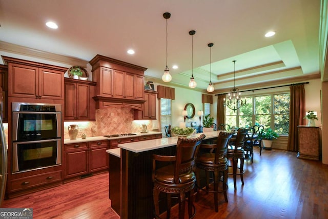 kitchen featuring dark wood-type flooring, light countertops, appliances with stainless steel finishes, backsplash, and a tray ceiling