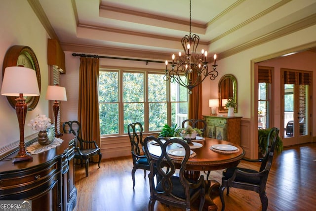 dining space with a tray ceiling, a chandelier, wood finished floors, and ornamental molding