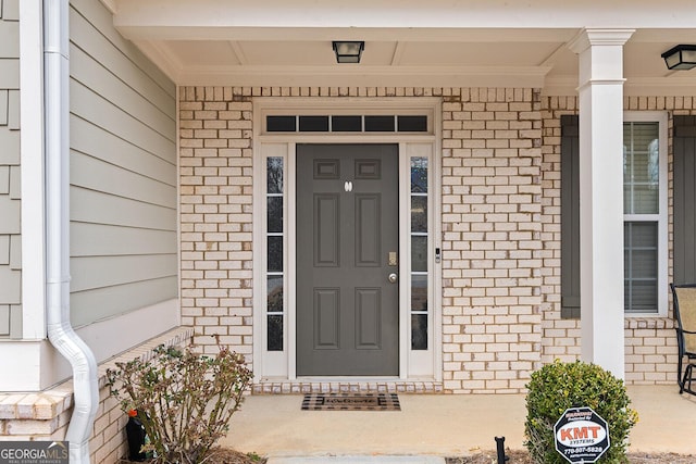 view of exterior entry with a porch and brick siding