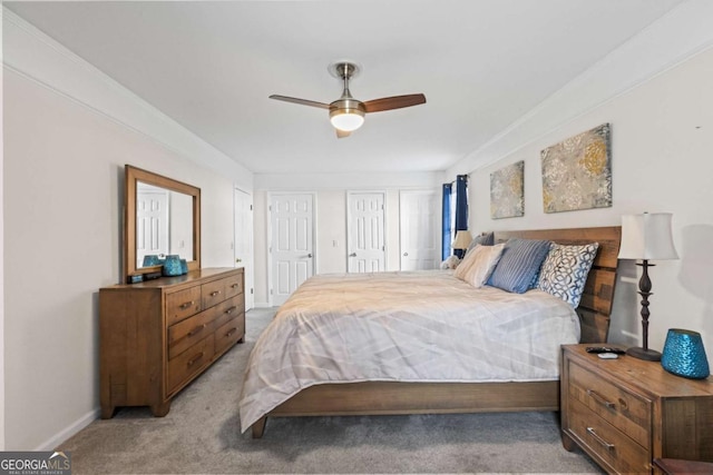 bedroom featuring a ceiling fan, light carpet, baseboards, and two closets