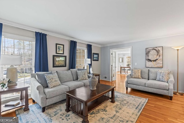 living area featuring crown molding, baseboards, visible vents, and light wood-style floors