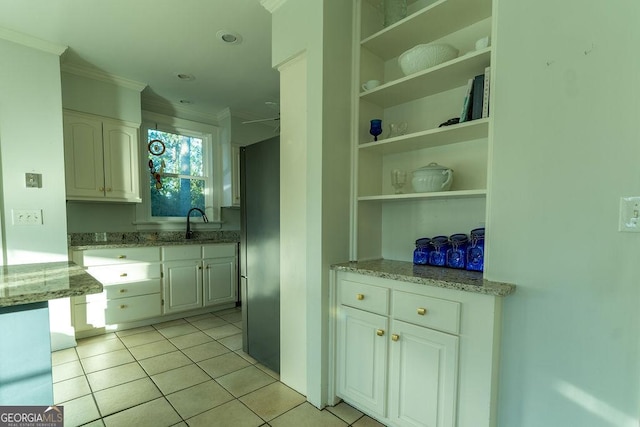 kitchen with light tile patterned floors, light stone counters, a sink, white cabinetry, and open shelves