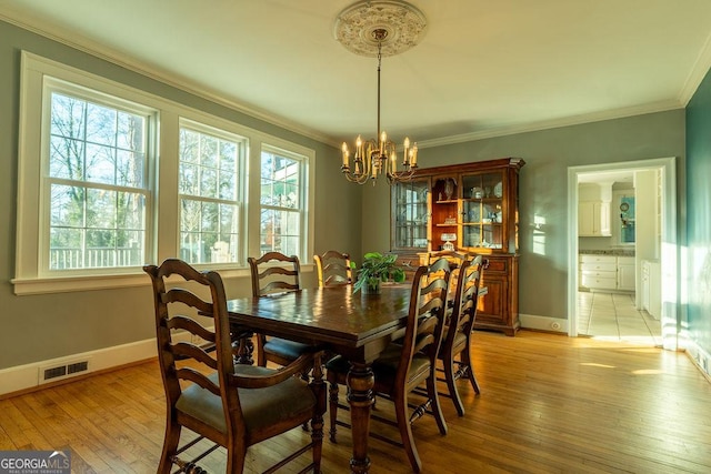 dining room with light wood finished floors, visible vents, ornamental molding, a chandelier, and baseboards