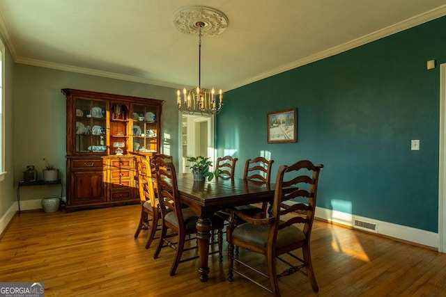 dining space with an inviting chandelier, crown molding, visible vents, and wood finished floors