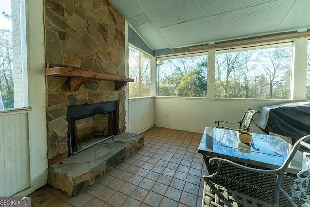 sunroom with lofted ceiling, a stone fireplace, and a healthy amount of sunlight