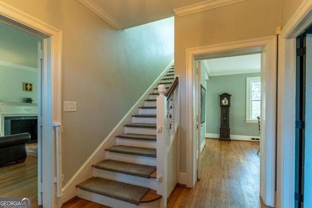 stairs with baseboards, visible vents, ornamental molding, wood finished floors, and a fireplace