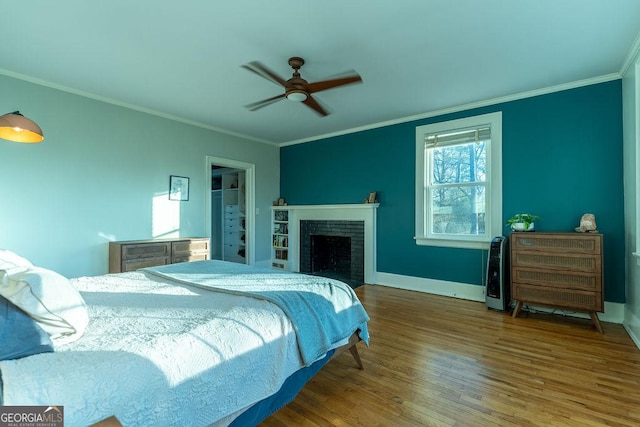 bedroom featuring a fireplace, ornamental molding, ceiling fan, wood finished floors, and baseboards