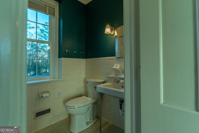 half bathroom featuring visible vents, toilet, a sink, tile patterned flooring, and tile walls