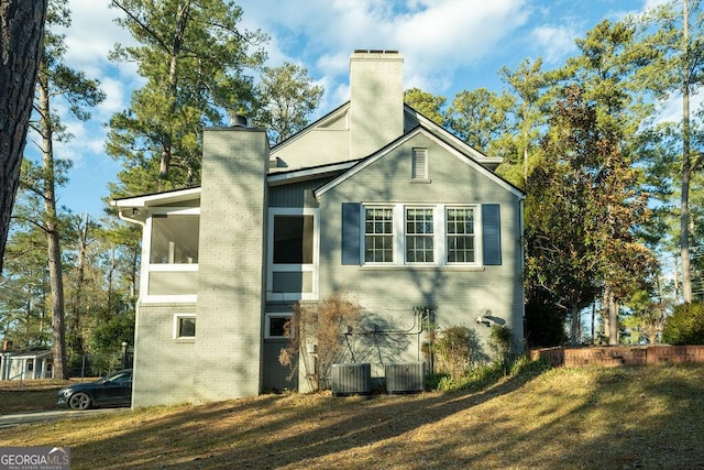 view of side of property featuring a chimney, central AC, and brick siding