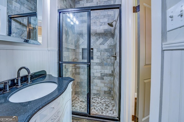 bathroom with a wainscoted wall, a shower stall, and vanity