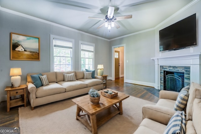 living room with ornamental molding, a ceiling fan, a stone fireplace, wood finished floors, and baseboards