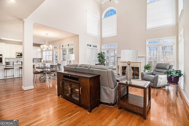 living room featuring baseboards, a glass covered fireplace, light wood-type flooring, ornate columns, and a chandelier