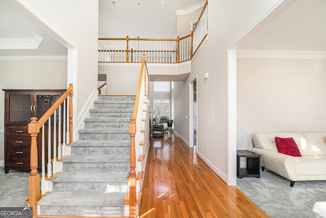 stairs with baseboards, wood finished floors, a towering ceiling, and crown molding