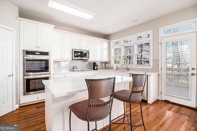 kitchen with tasteful backsplash, appliances with stainless steel finishes, white cabinetry, a sink, and wood finished floors