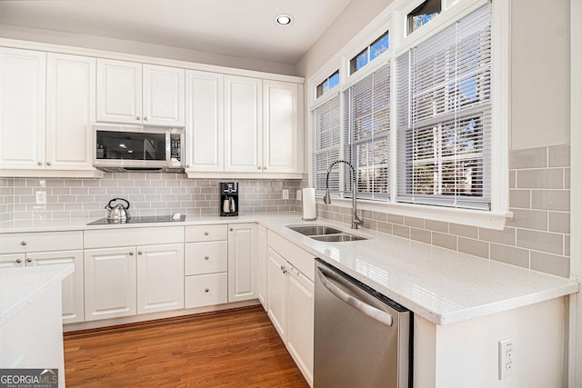 kitchen with light wood-style flooring, stainless steel appliances, a sink, white cabinetry, and decorative backsplash