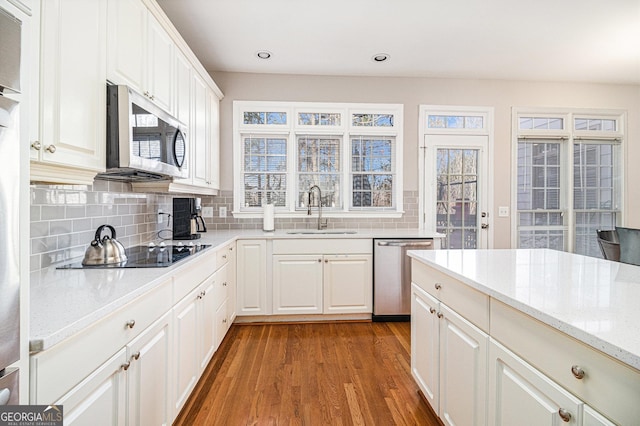 kitchen with stainless steel appliances, decorative backsplash, white cabinets, a sink, and wood finished floors