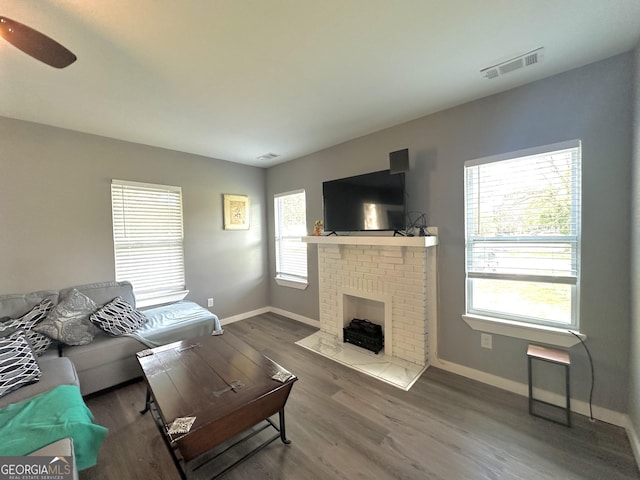 living room with visible vents, a fireplace, baseboards, and wood finished floors