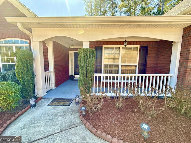 view of exterior entry with a porch and brick siding