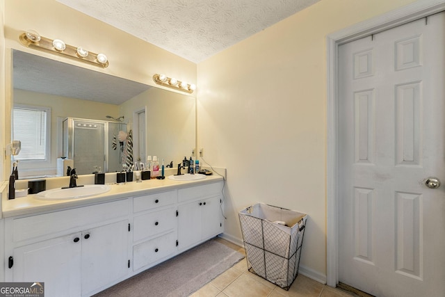 bathroom with double vanity, a stall shower, a sink, a textured ceiling, and tile patterned floors