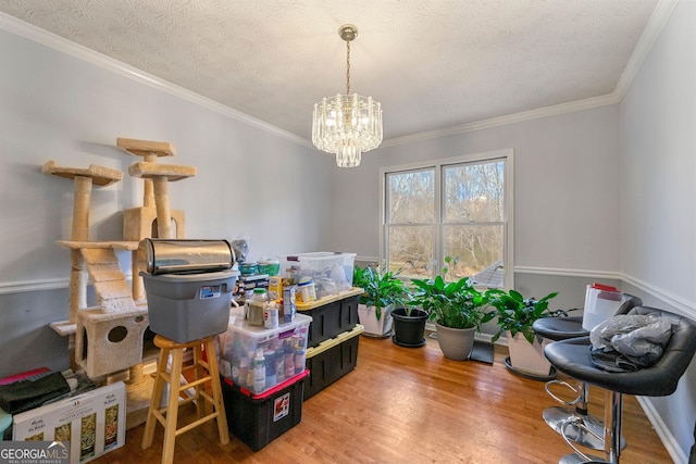 dining area featuring a textured ceiling, ornamental molding, wood finished floors, and a notable chandelier