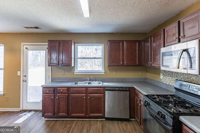 kitchen featuring baseboards, visible vents, dark wood-type flooring, stainless steel appliances, and a sink