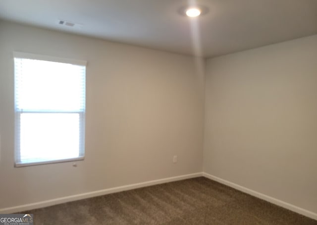 empty room featuring dark colored carpet, a wealth of natural light, and baseboards